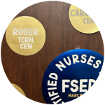 Circular, blue and gold Certified Nurses Day decorations with the names and credentials of certified nurses on a wooden background.