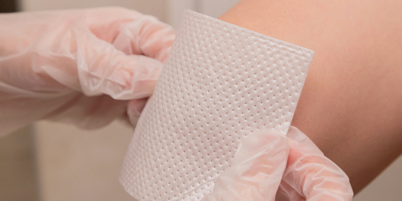 Gloved hands apply a white sterile medical gauze pad to a person's arm.