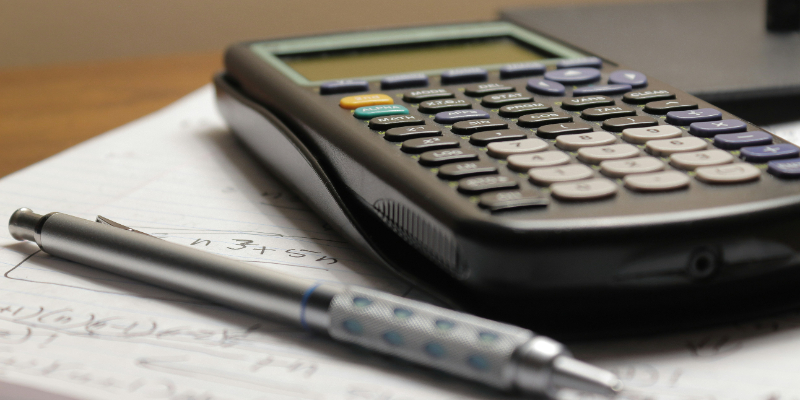 A calculator and pen rest on top of handwritten notes with mathematical equations.