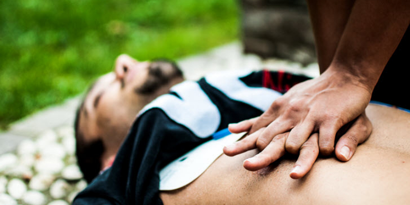 Person performing chest compressions on an individual lying on the ground, demonstrating CPR in an outdoor setting.