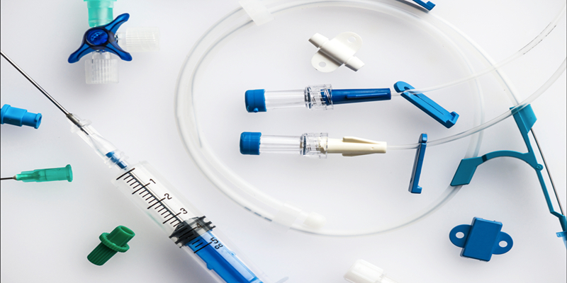 Medical supplies including a syringe, tubing, connectors, and valves are arranged on a white surface.
