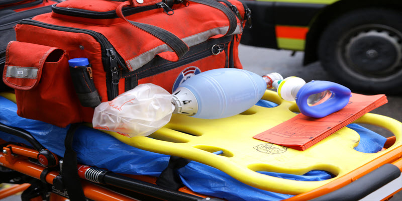 A medical bag, manual resuscitator, and airway mask are placed on a yellow stretcher, prepared for emergency use.