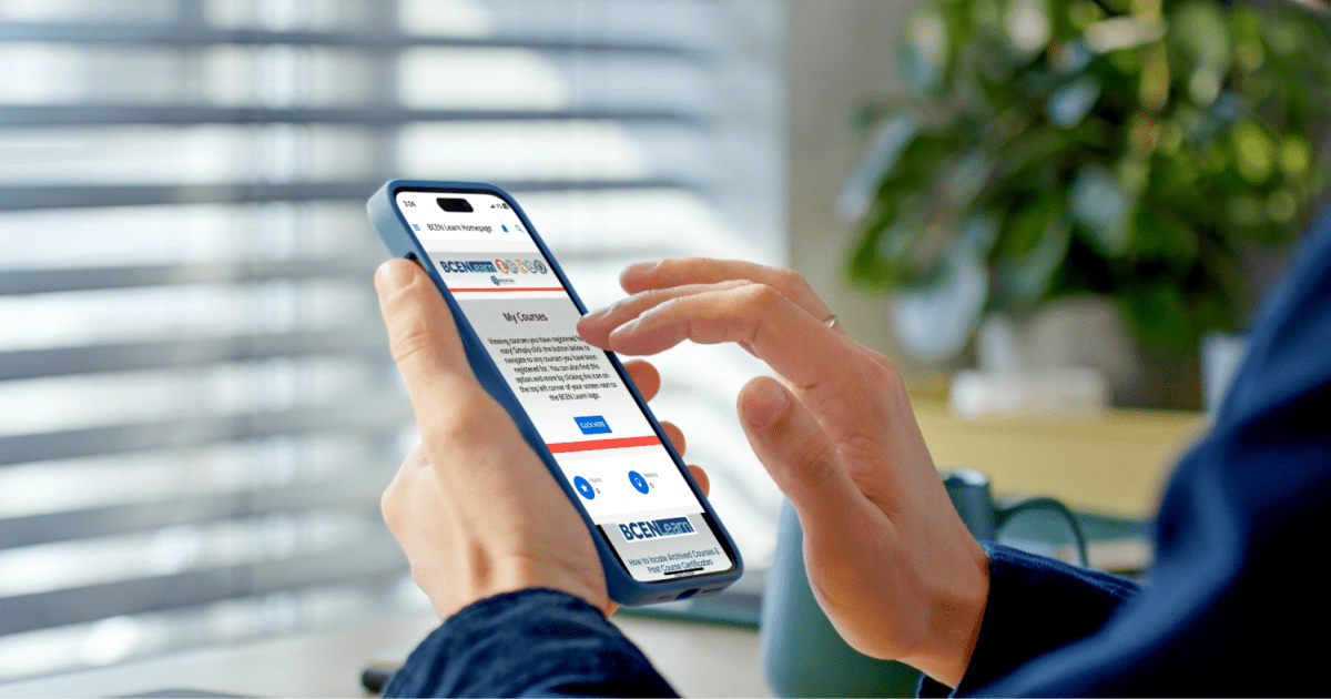 A person holds a smartphone and interacts with a job application website; the background shows a blurred office setting with a plant and a cup.