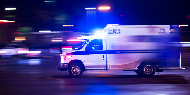 An ambulance with flashing lights drives quickly through a city street at night.