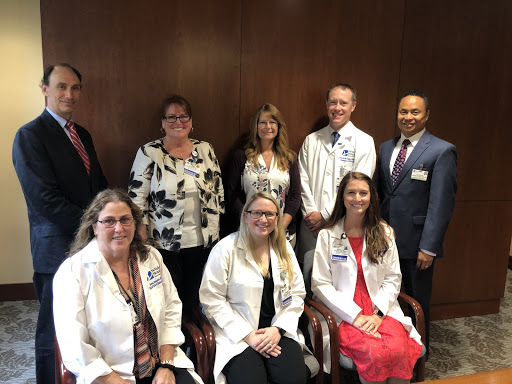 Eight professionals, including five in white lab coats and three in business attire, pose together in a formal indoor setting with wood-paneled walls.