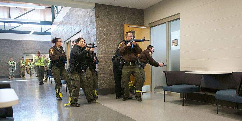 A group of law enforcement officers with rifles enter a building hallway in a coordinated manner during a training exercise.