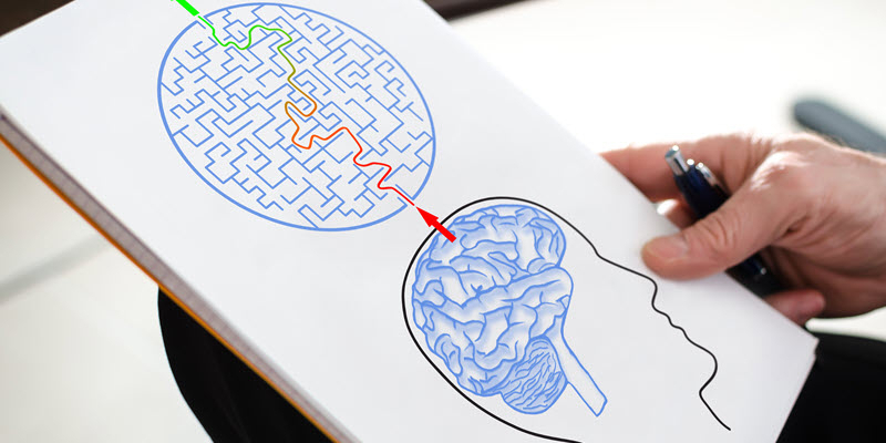 A person holds a paper showing a human head with a brain, connected by a colored line to a circular maze above the head.