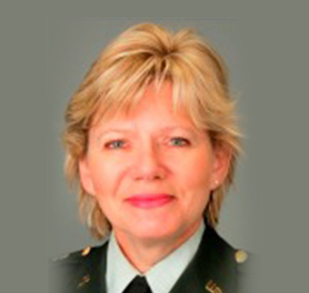 Portrait of a woman in a military uniform with short blonde hair, facing forward and smiling slightly, against a plain grey background.