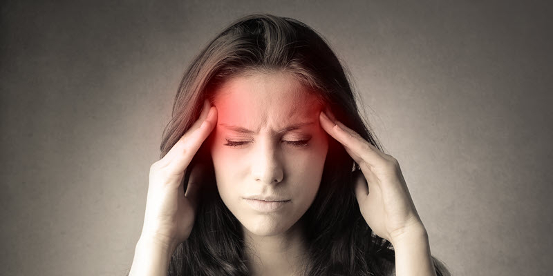 A woman holding her temples with closed eyes, appearing to have a headache; red highlights on her temples suggest pain or discomfort.