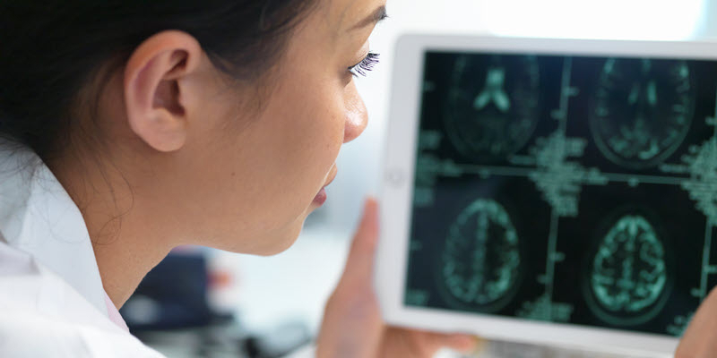 A person examines brain scan images displayed on a tablet.