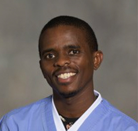 A person wearing a light blue medical scrub top smiles at the camera against a neutral background.