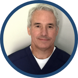 A middle-aged man with short gray hair wearing a dark blue shirt and white undershirt, facing the camera against a plain background.