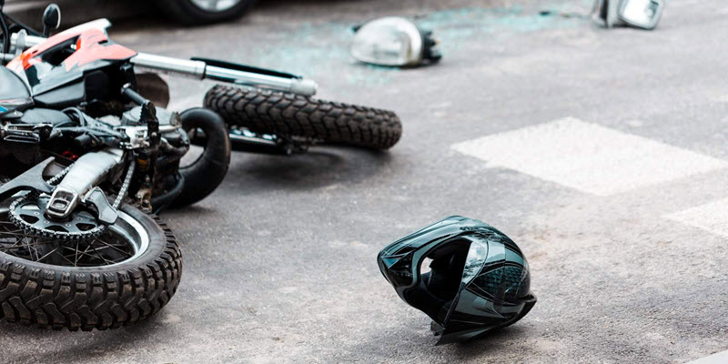 A motorcycle lies on its side on the road with a helmet next to it and broken glass scattered nearby, suggesting an accident scene.