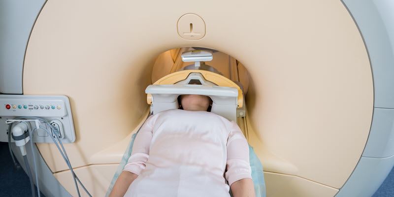A person lies on a table entering an MRI machine, prepared for a medical scan with their head positioned inside the scanner.