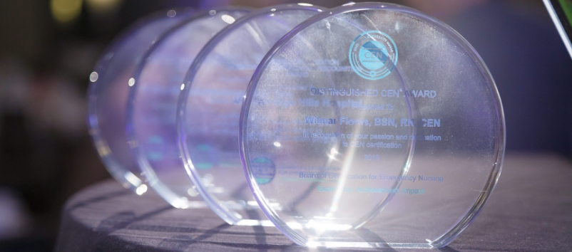 Four clear, round glass awards with engraved text are displayed in a row on a table, with one award in sharp focus and the others blurred in the background.