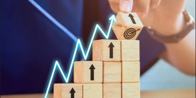 A hand stacking wooden blocks with upward arrows and a target symbol, alongside a rising graph line, representing growth and goal achievement.