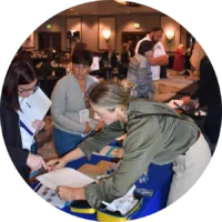Several people interact at a display table during an emergency nursing conference; one woman is signing a document at the sponsor exhibitor booth while others observe.