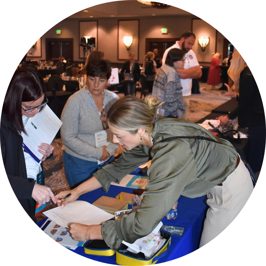 Several people interact at a display table during an emergency nursing conference; one woman is signing a document at the sponsor exhibitor booth while others observe.