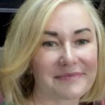 A woman with short blonde hair and light skin smiles softly at the camera.
