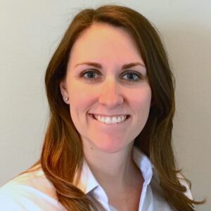 A woman with long brown hair, wearing a white collared shirt, smiles at the camera in front of a plain light-colored background—her confident poise reflects the professionalism of BCEN conference speakers.