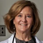 A woman with shoulder-length light brown hair smiles at the camera, wearing a white coat and a stethoscope around her neck.