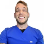 A person wearing blue medical scrubs smiles at the camera against a plain white background.