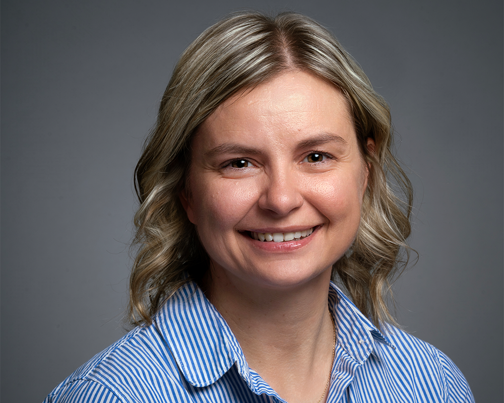 A woman with shoulder-length blonde hair and a blue striped shirt smiles at the camera against a plain gray background, representing the excellence of the 2026 BCEN Distinguished Award Winners.