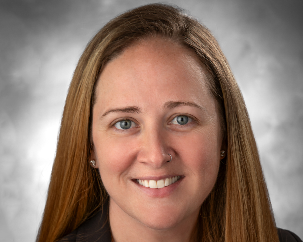 A woman with straight light brown hair, light eyes, and a nose piercing, smiling at the camera against a gray background—one of the 2026 BCEN Distinguished Award Winners.