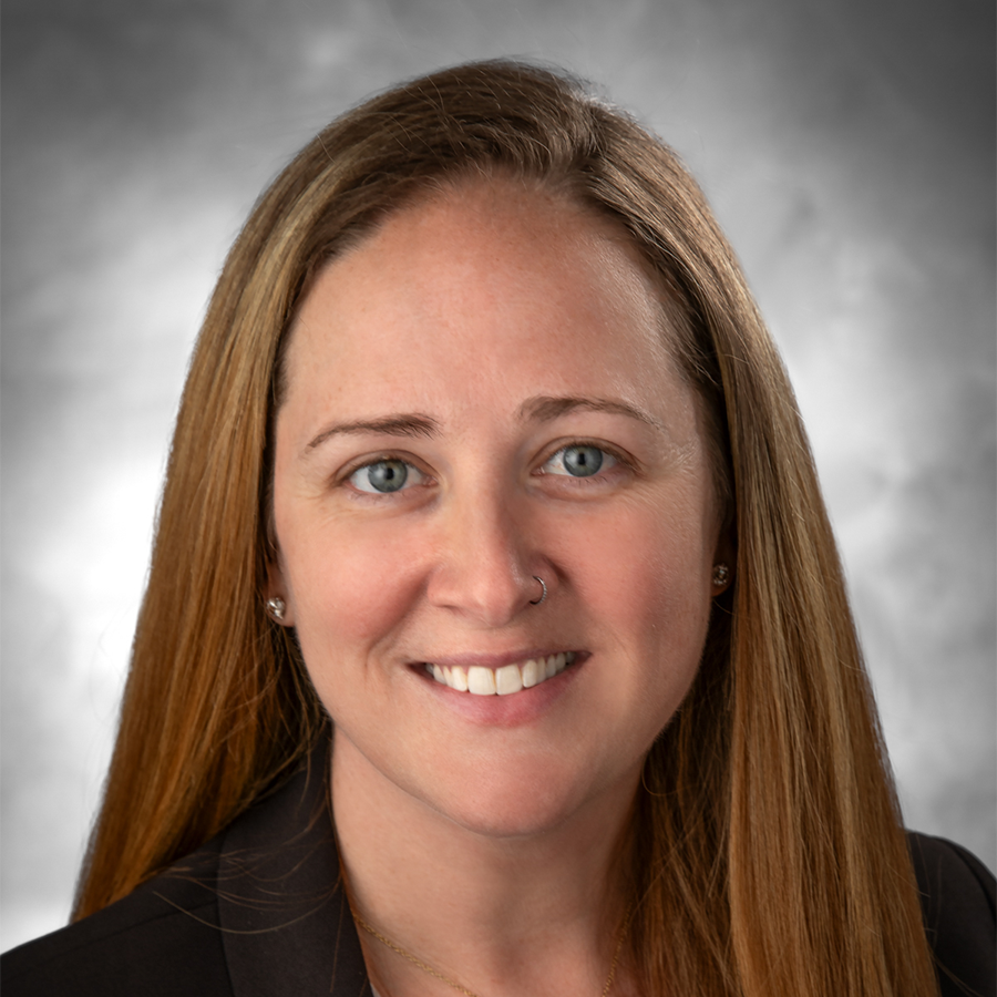 A woman with long light brown hair, wearing a dark blazer, is smiling in front of a gray, softly blurred background. She is the 2026 Distinguished TCRN Award Winner.