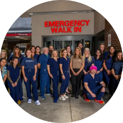 A group of healthcare workers and staff stand and pose outside an emergency walk-in entrance at a medical facility.