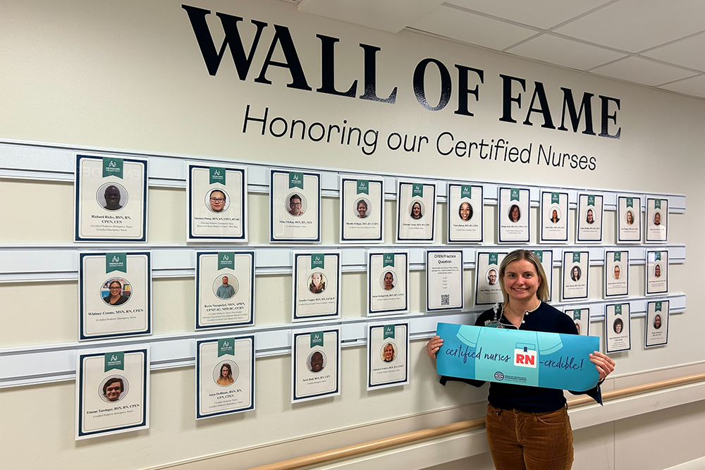 A woman holds a banner reading "Certified Nurses RNcredible" in front of a Wall of Fame, which highlights certified nurses and the 2026 Distinguished CPEN Award Winner.
